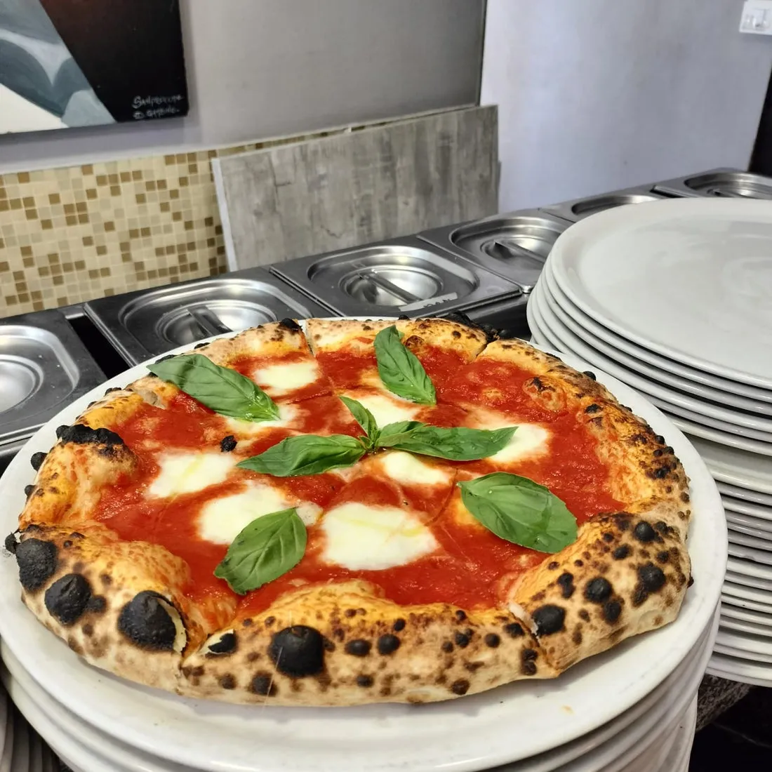 Pizza margherita con cornicione alto e macchiato, sul bancone della pizzeria